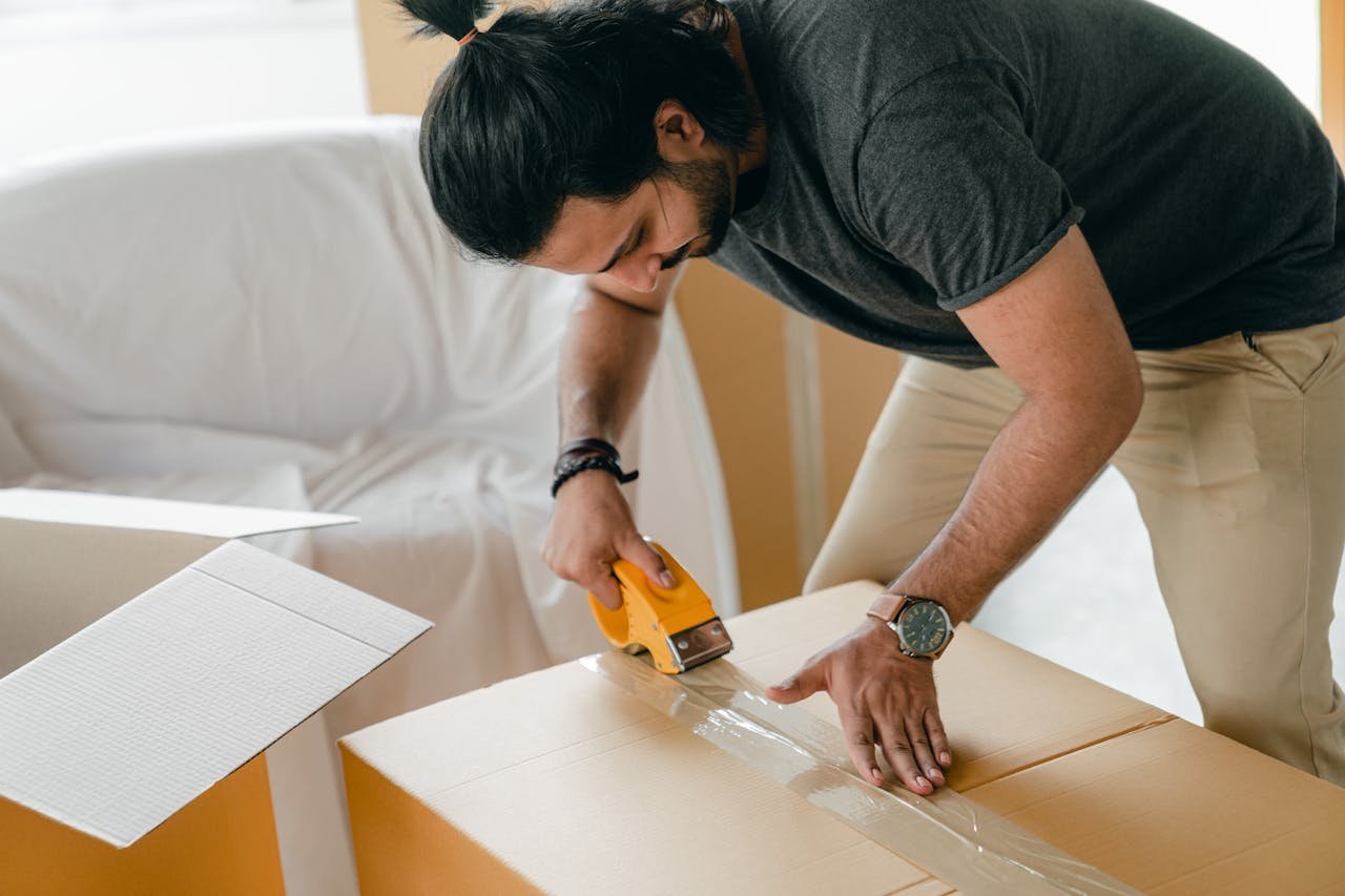 A man packing boxes with tape, preparing to move into a new home.