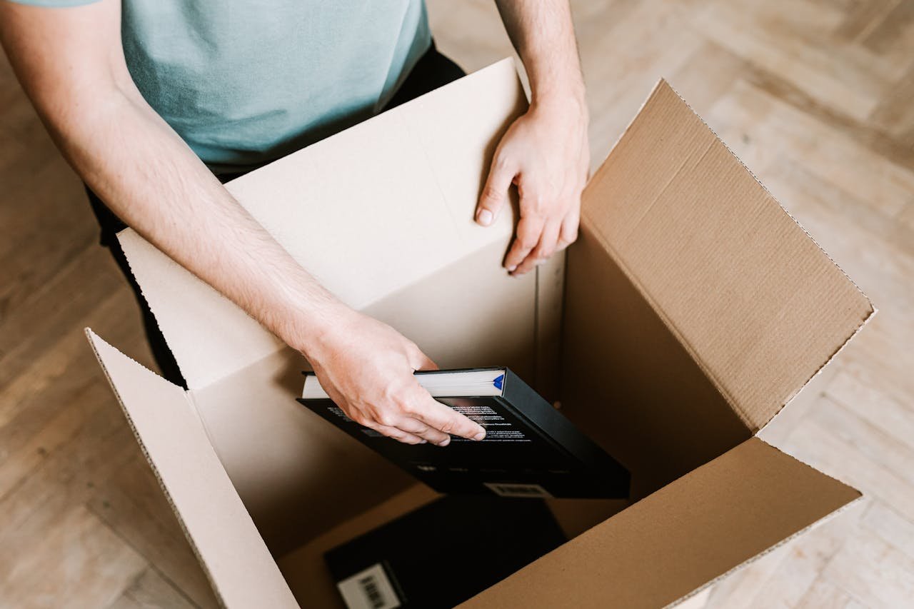 Man organizing and packing books in a cardboard box at home, perfect for moving or storage themes.